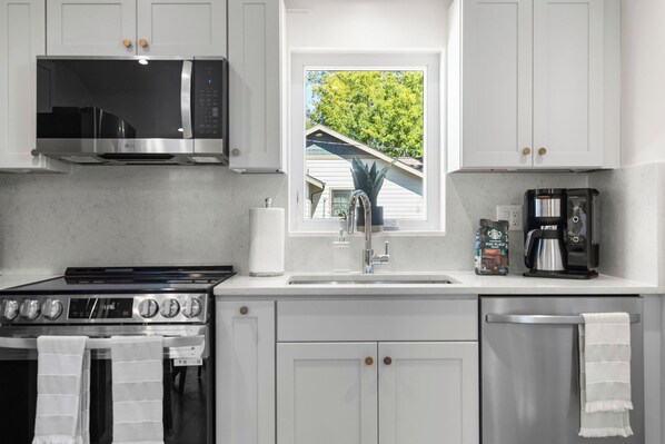 A modern kitchen with white cabinets, a stainless steel microwave, a stove, a sink, and a coffee maker. - Walkable 2BR Close to downtown, hiking, Red Rocks (Denver)