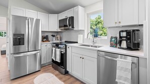A modern kitchen with stainless steel appliances, white cabinetry, and a large window providing natural light. - Walkable 2BR Close to downtown, hiking, Red Rocks (Denver)