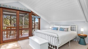 A bedroom with a large bed, a nightstand, a bench, and a view of the outdoors through a sliding glass door.
