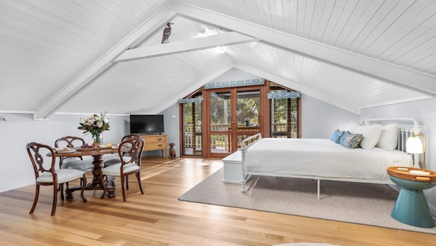 A spacious attic bedroom with a large bed, a desk with chairs, and a television.