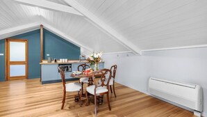 A dining area with a wooden table and chairs, a kitchen with a microwave, and a white radiator.