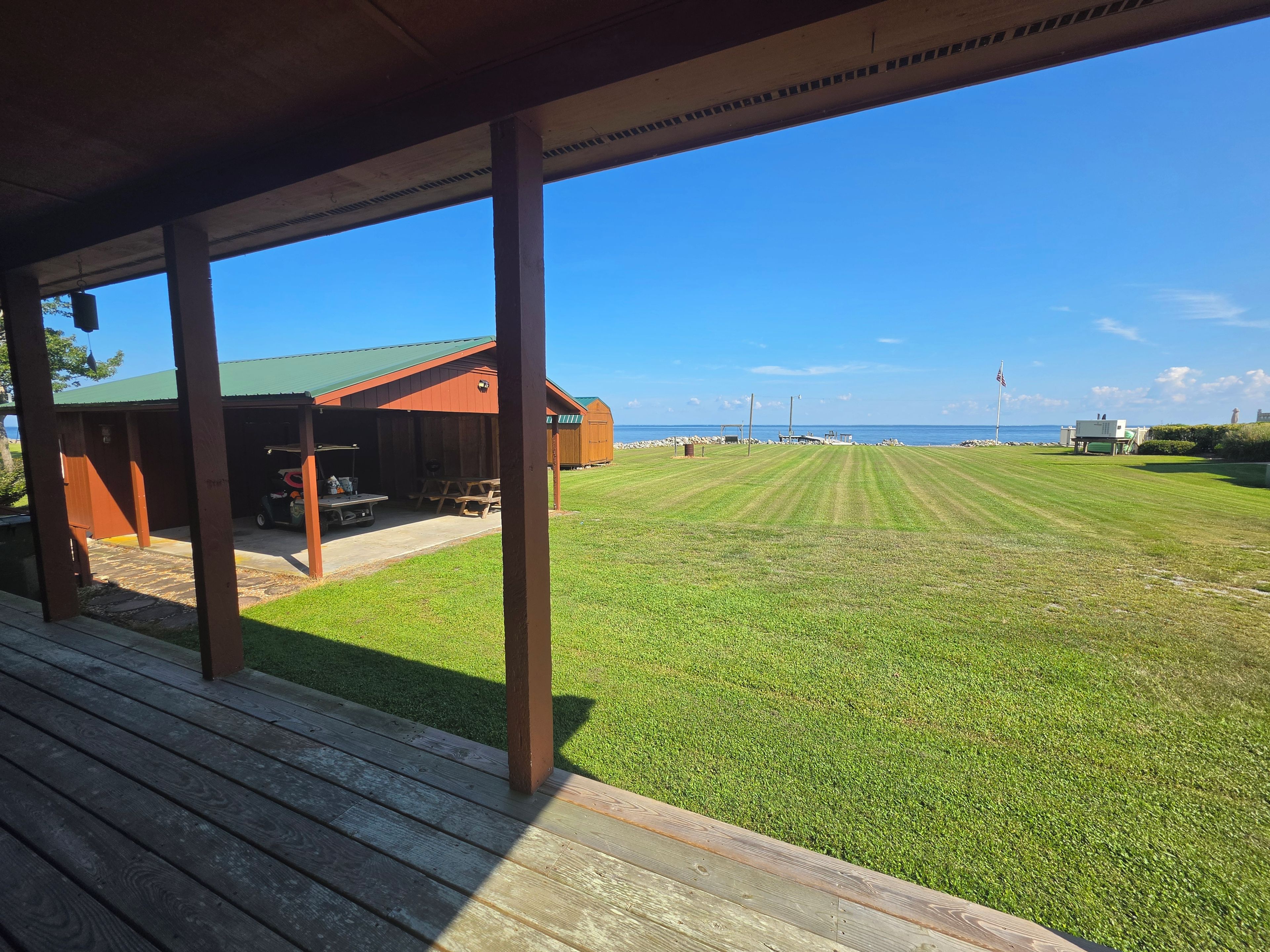 A covered outdoor area with a grassy lawn, wooden deck, and a building with a green roof.