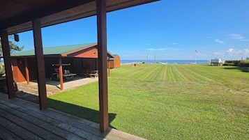 A covered outdoor area with a grassy lawn, wooden deck, and a building with a green roof.