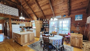 A rustic wooden interior with a kitchen, dining area, and a large window.