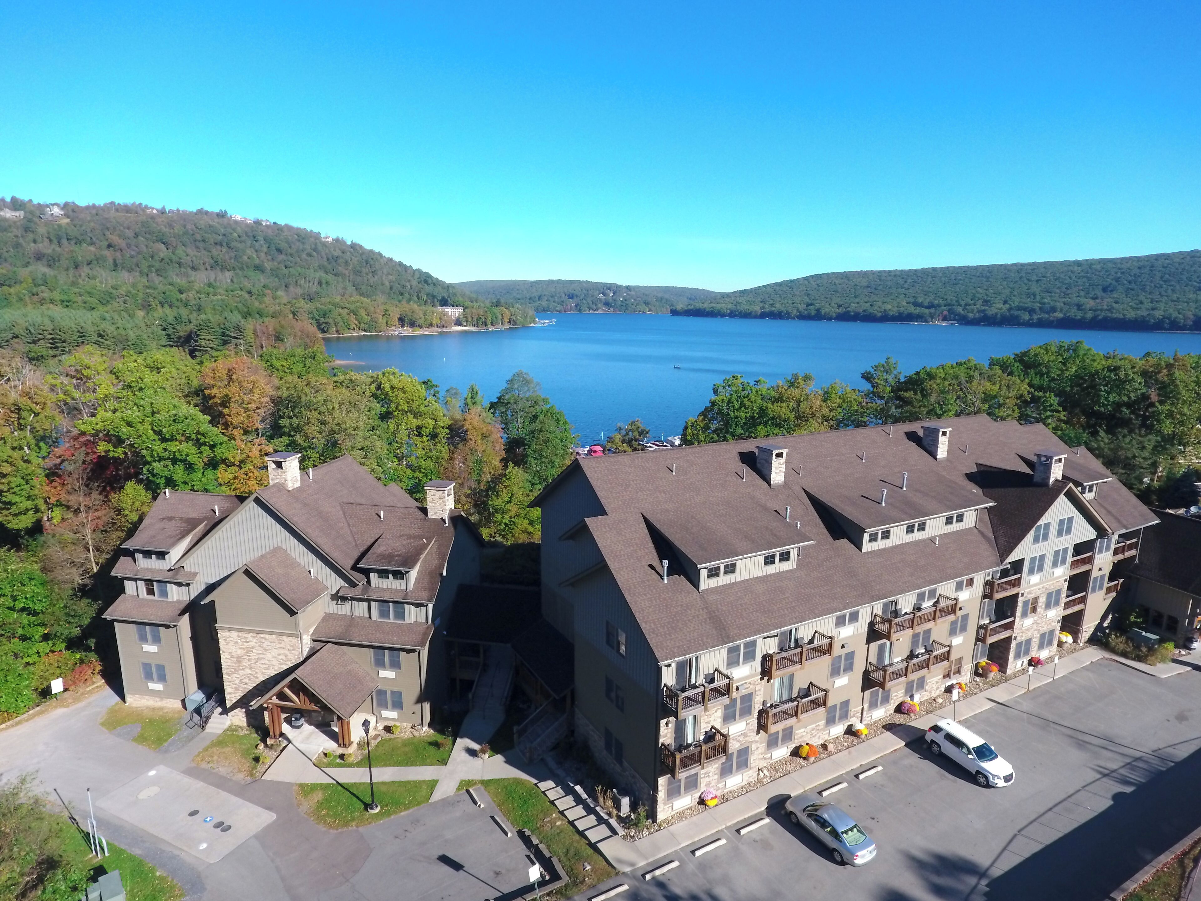 A multi-story building with balconies, a parking lot, and a view of a lake.