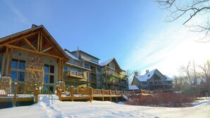 Un lodge a più piani con facciata in pietra, balconi in legno e terreno innevato.