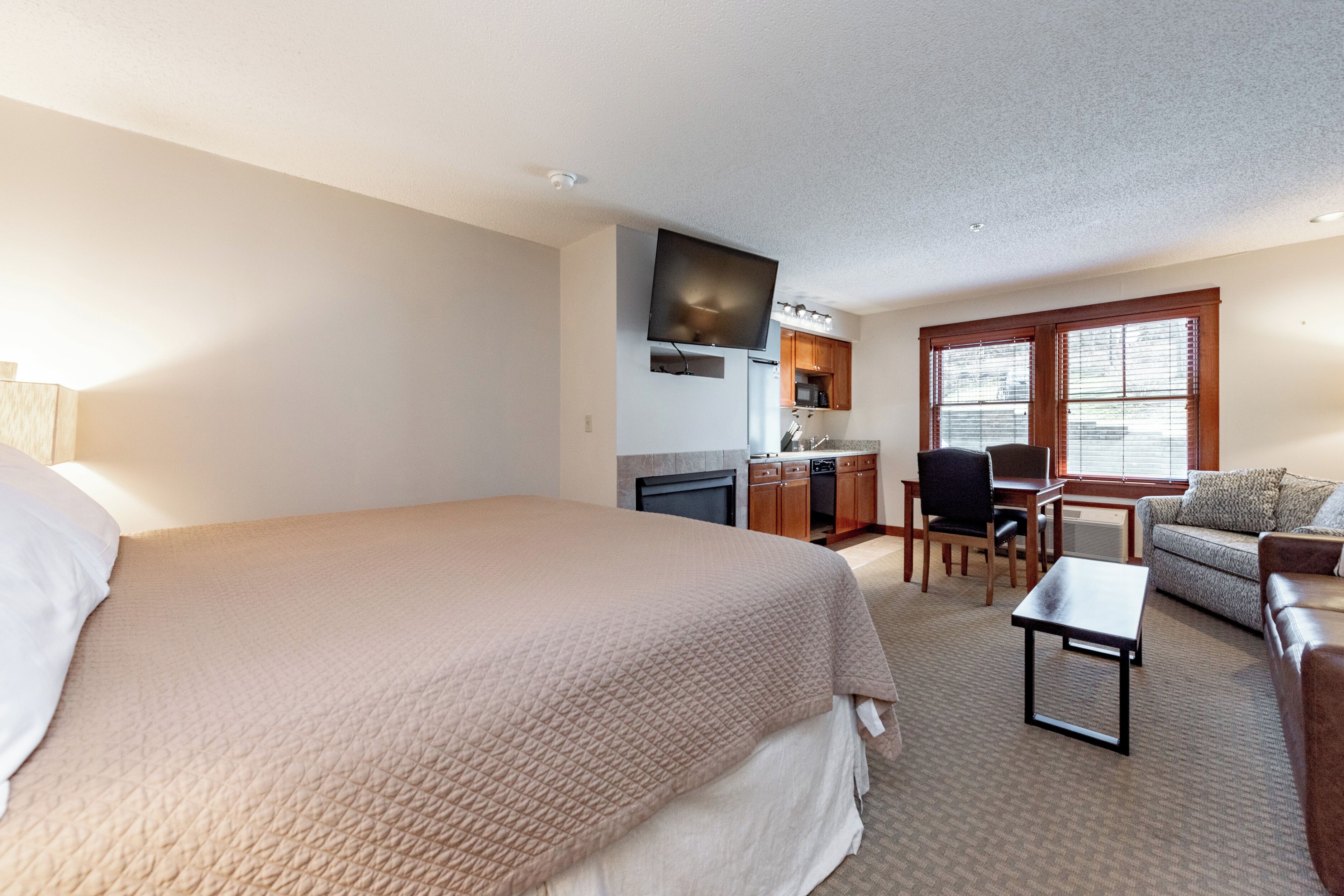 A hotel room with a large bed, a desk with a chair, a sofa, and a television mounted on the wall.