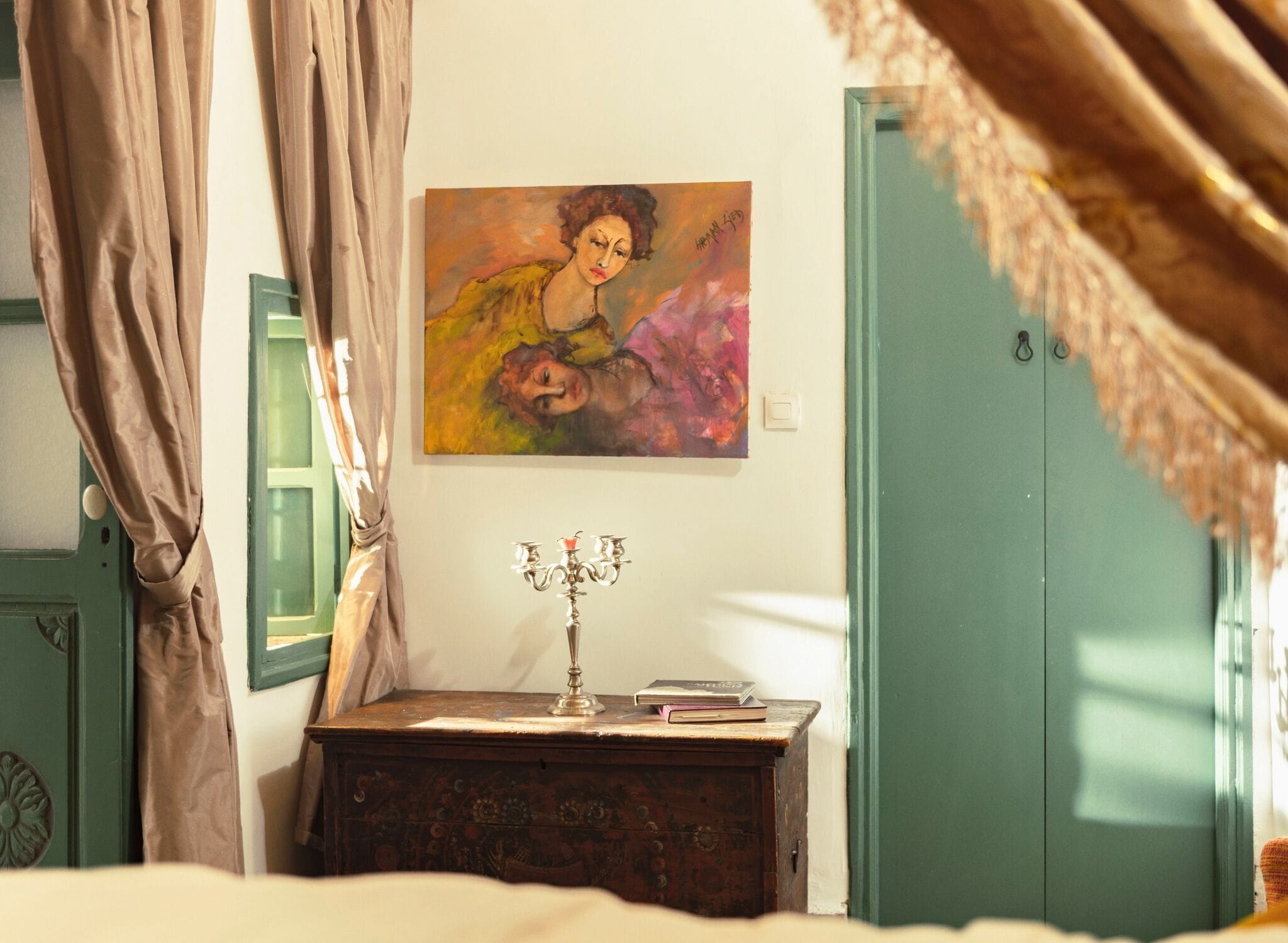 Une chambre à coucher avec un lit, une table de chevet surmontée d’un chandelier, un tableau et une armoire verte.