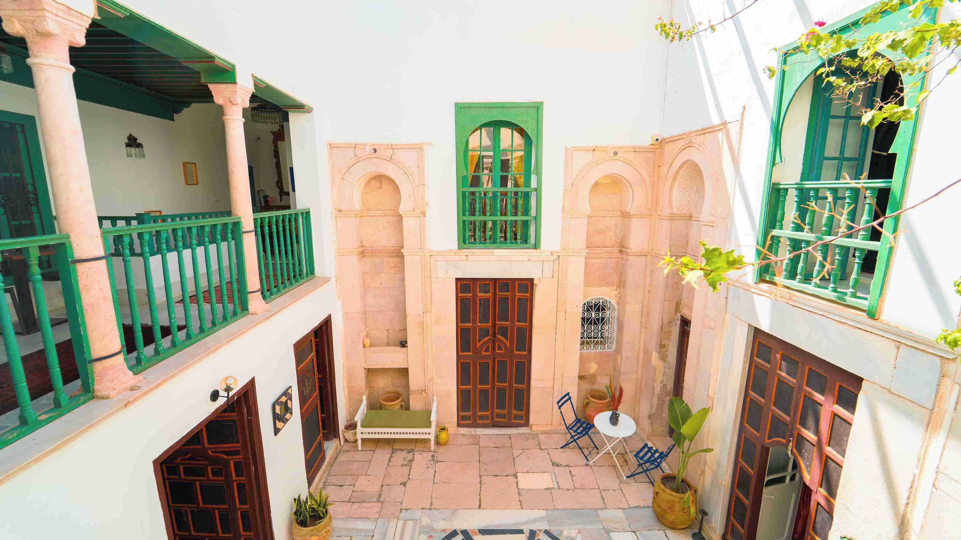 A courtyard with a central door, two balconies, and a small table with chairs.