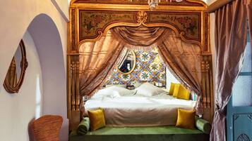 Un dormitorio con una cama grande, dosel ornamentado, un espejo y una araña.