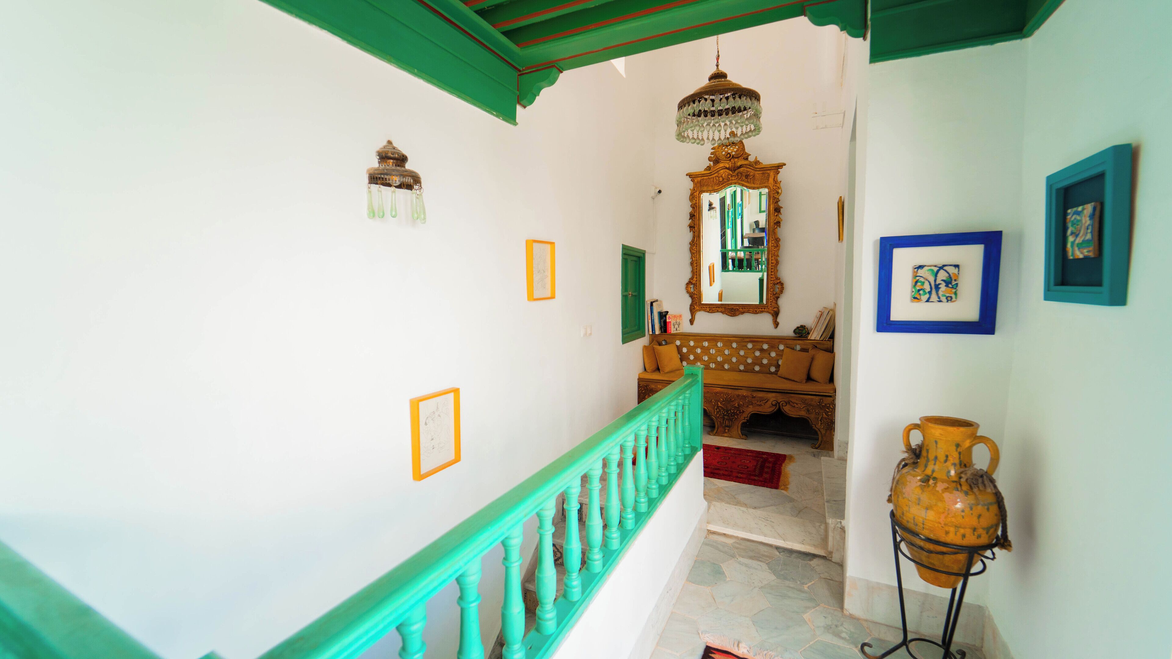 A staircase with green railings leading to a room with a wooden bench, a mirror, and a globe on a stand.