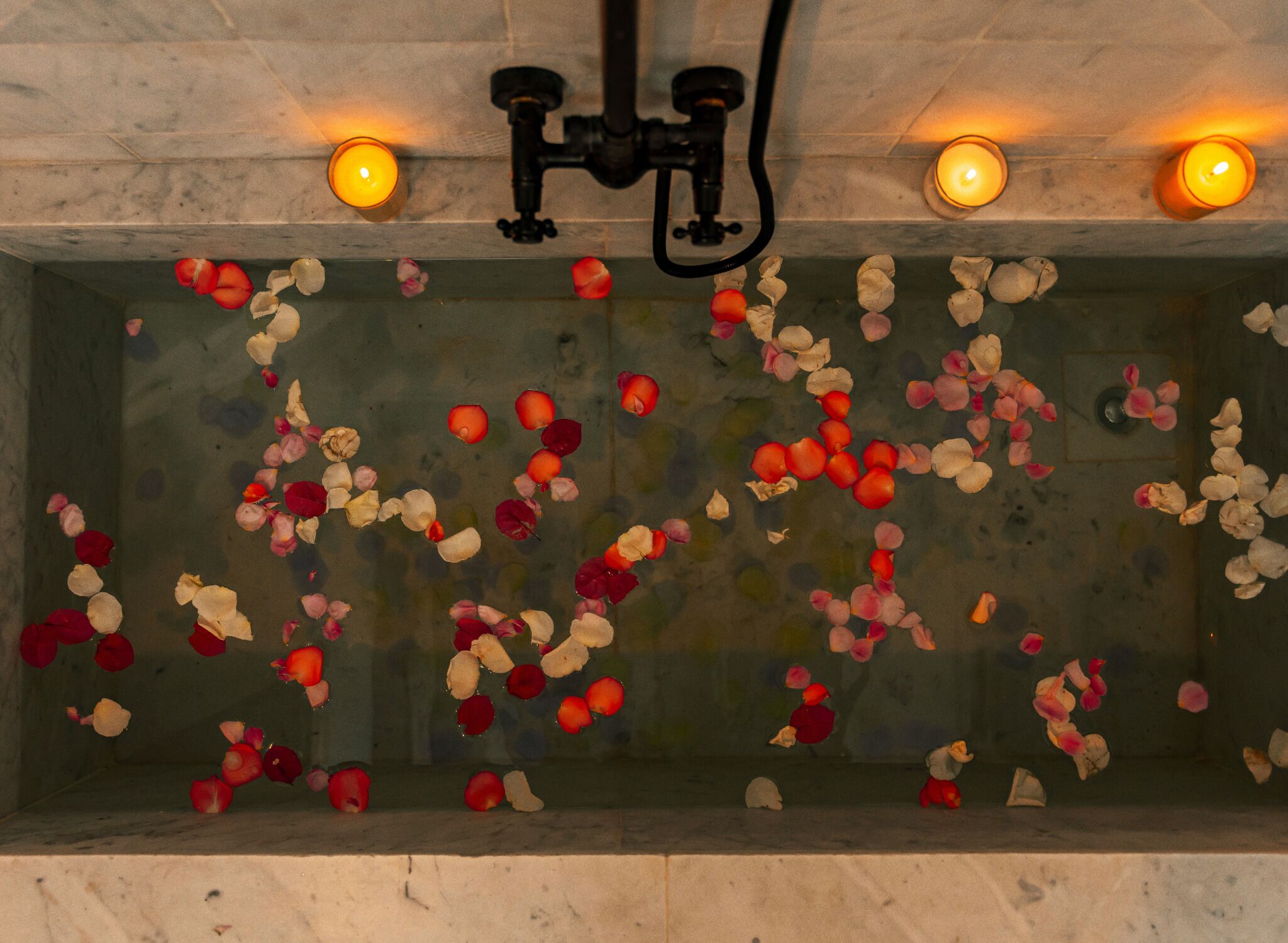 Una bañera llena de pétalos de rosa y dos velas encendidas.