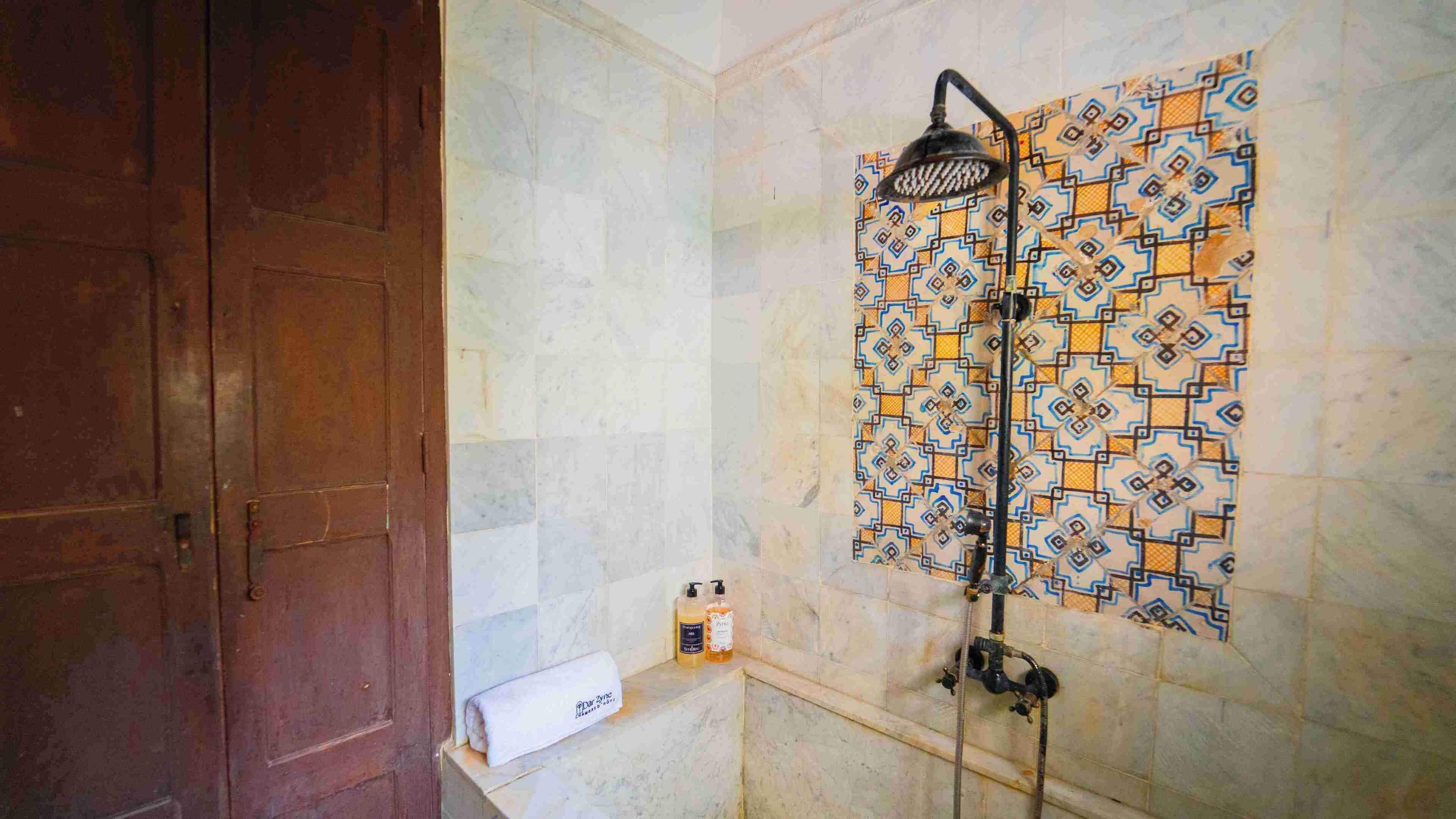 A bathroom with a shower, a towel dispenser, and a patterned tile wall.