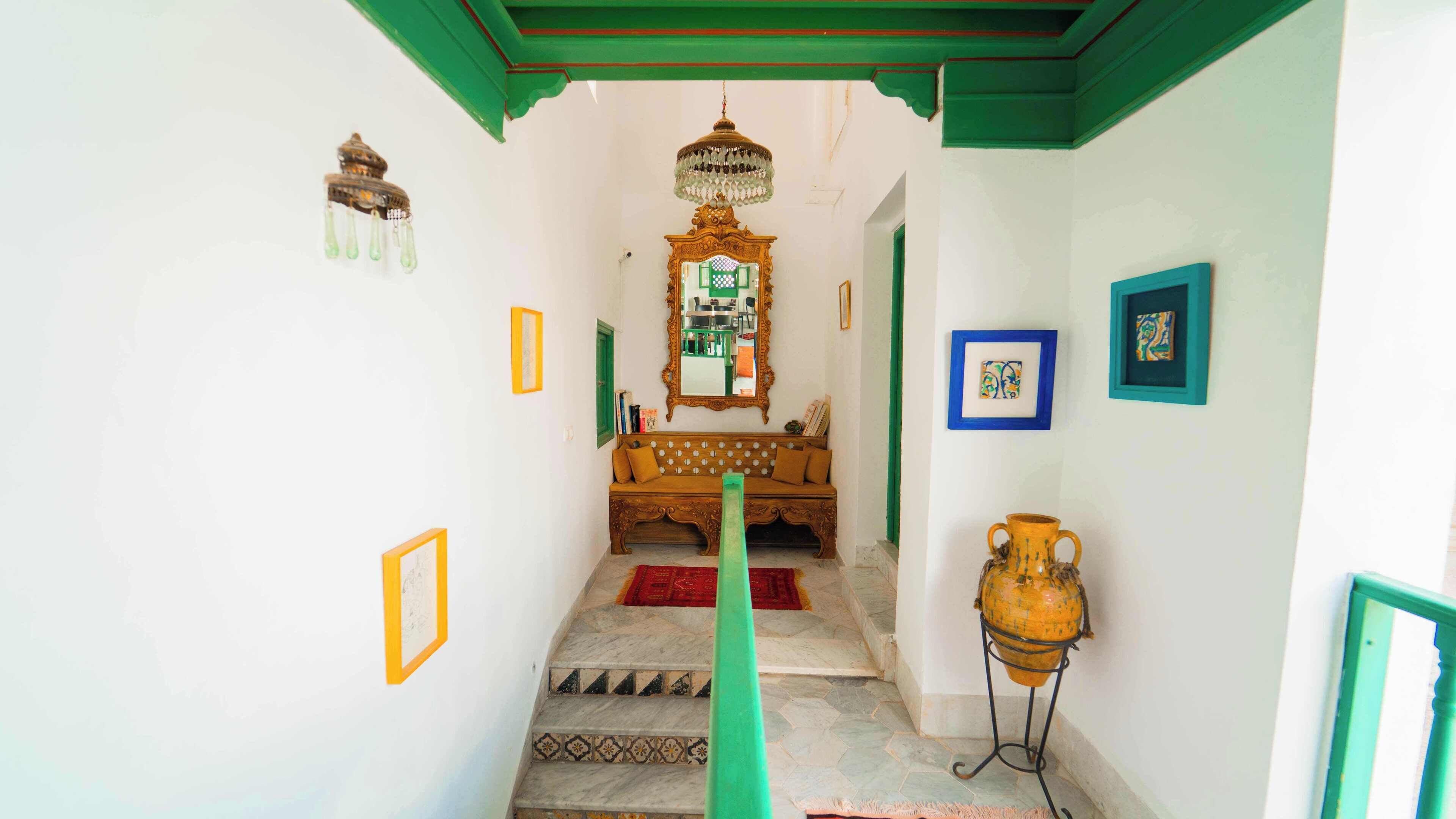 Un couloir étroit avec un banc en bois, un miroir et un vase posé sur un piédestal.
