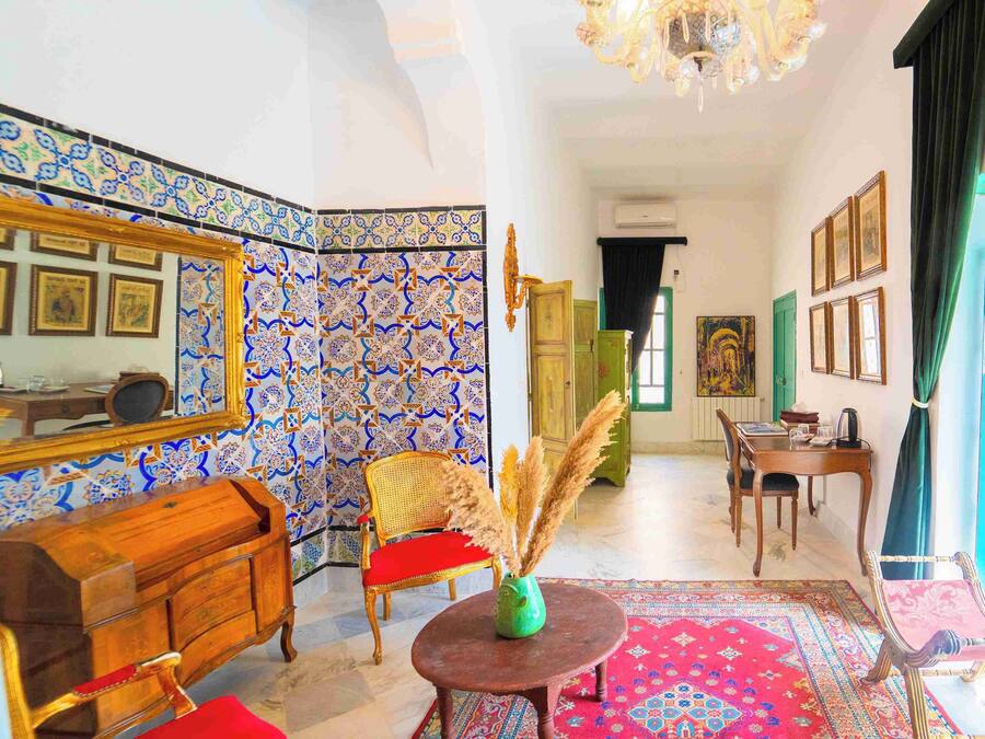 Una habitación con paredes de baldosas estampadas, un mueble de madera, una mesa de comedor con sillas y un ventanal con cortinas.