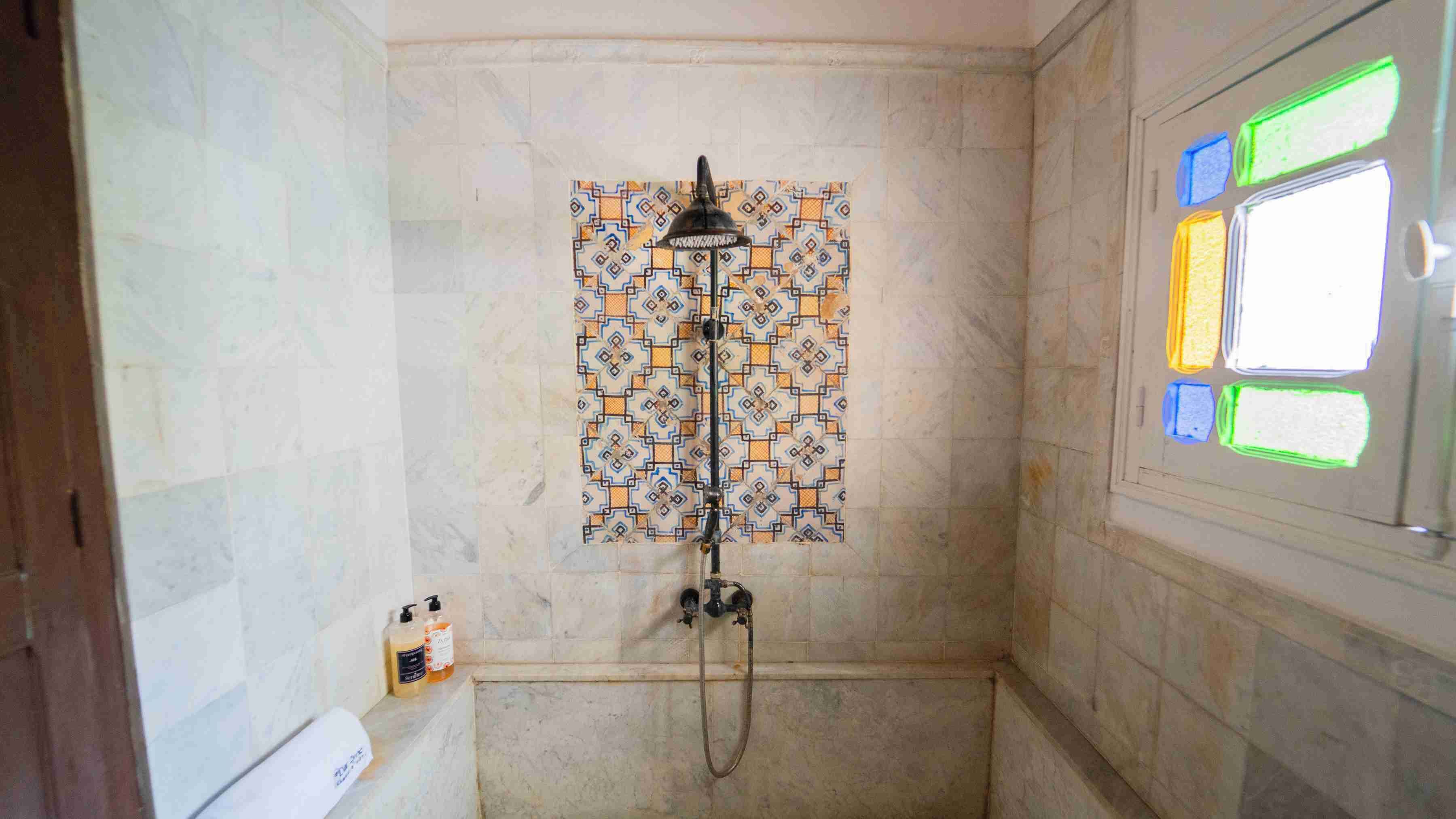 A bathroom with a shower, tiled walls, and a window with colored panes.