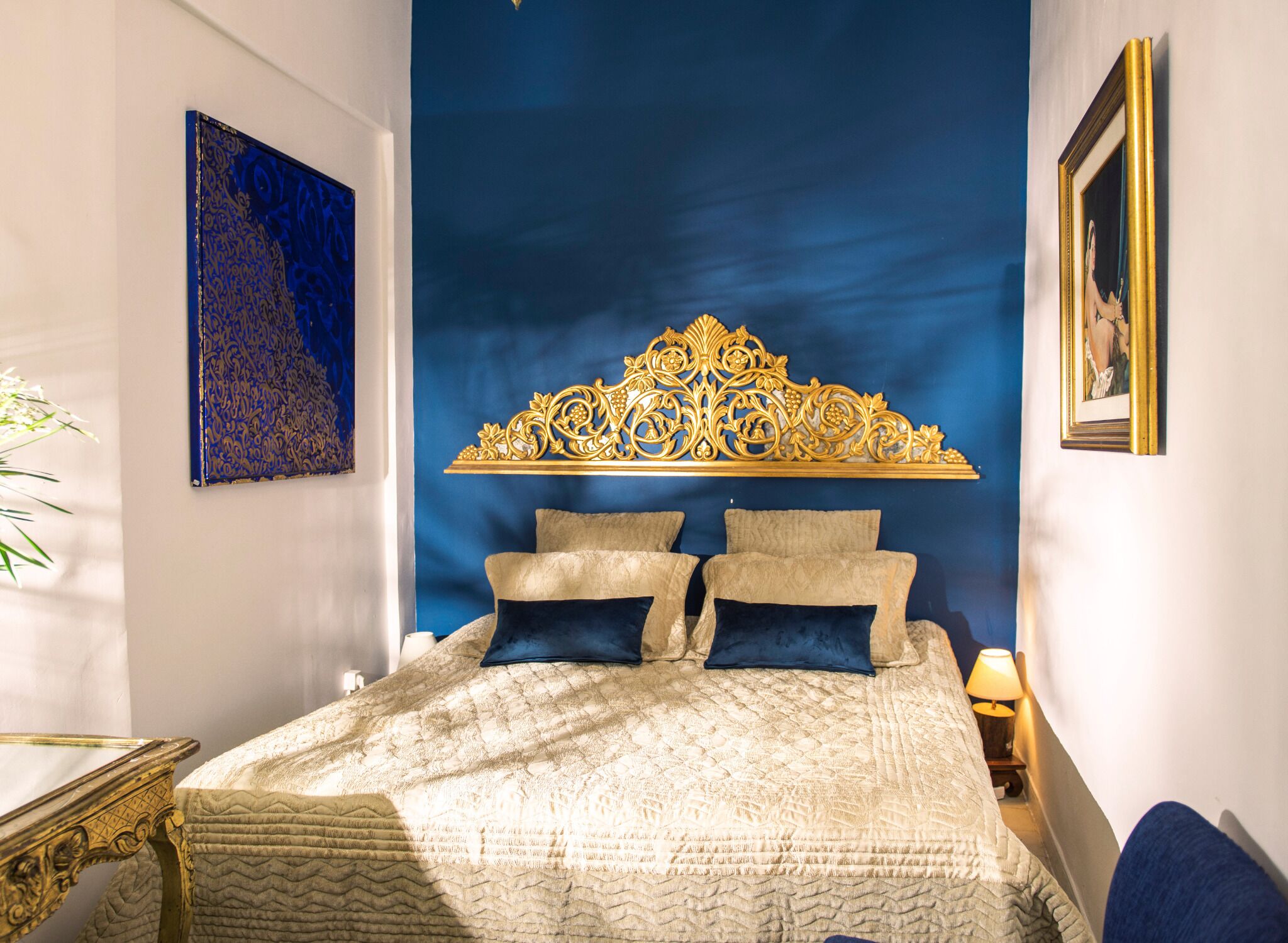 A bedroom with a large bed, a decorative headboard, a painting, and a framed picture on the wall.