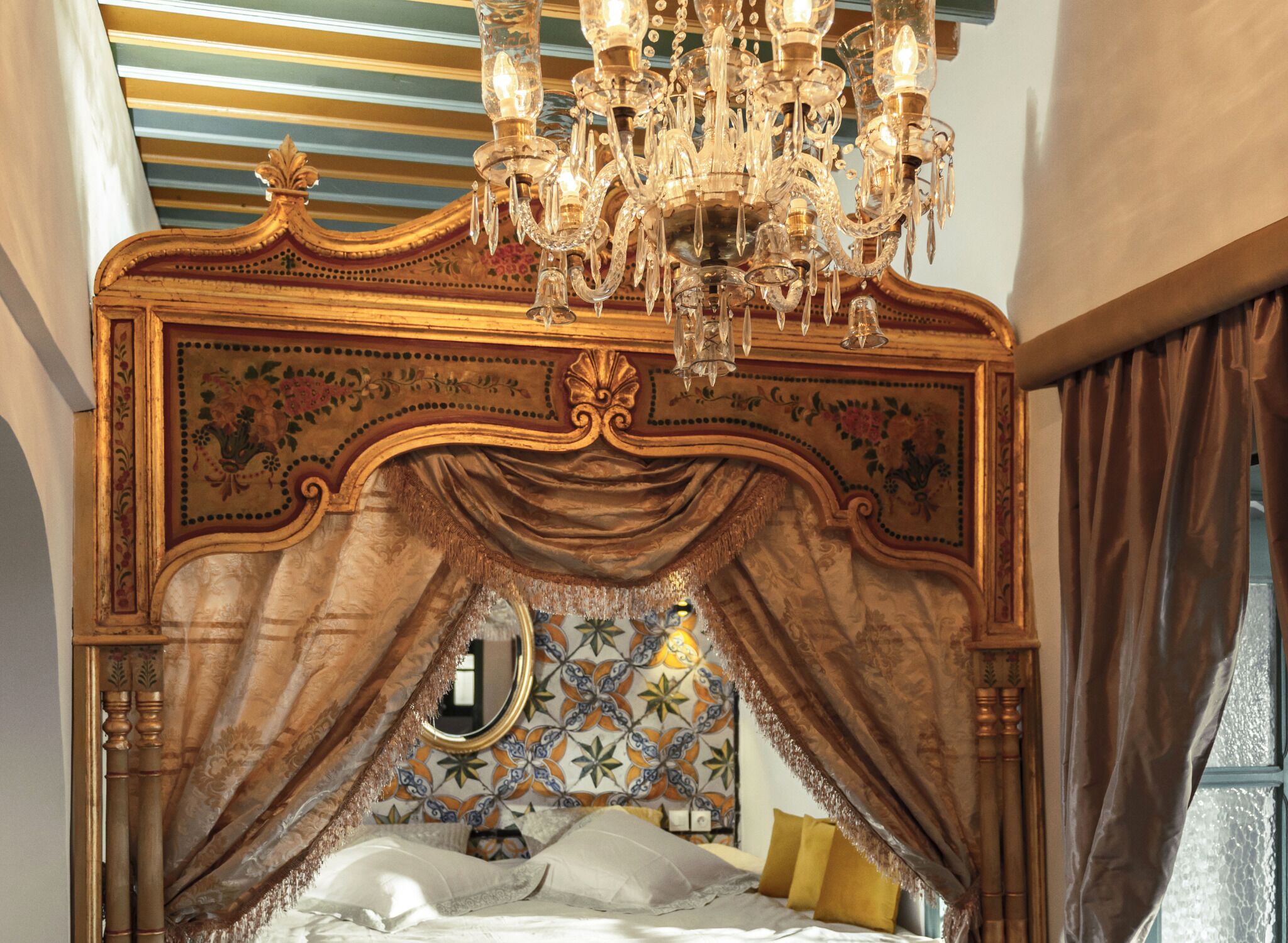 A bed with a canopy, a chandelier, and a floral-patterned wall.