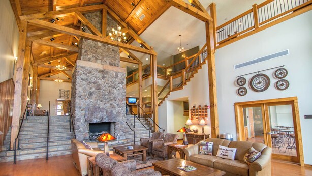 A spacious living area with a stone fireplace, wooden beams, a staircase, and a dining area. - Suites at Silver Tree: A212 One Bedroom Standard View (Oakland)