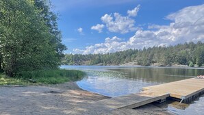 A lakeside view with a wooden dock extending into the water, surrounded by dense forest. - Modern Seaside Guesthouse with Stunning Archipelago Views (Stockholms län)