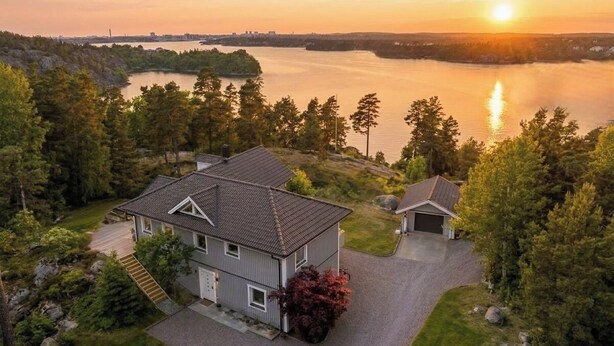 A two-story house with a garage, surrounded by trees and a lake. - Modern Seaside Guesthouse with Stunning Archipelago Views (Stockholms län)