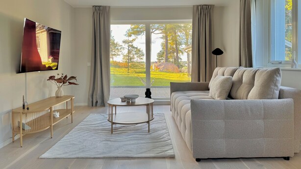 A modern living room with a sofa, a coffee table, a TV, and a view of a garden. - Modern Seaside Guesthouse with Stunning Archipelago Views (Stockholms län)