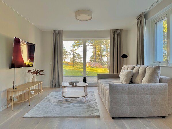 Uma sala de estar moderna com um sofá, uma mesa de centro, uma televisão e vista para um jardim.