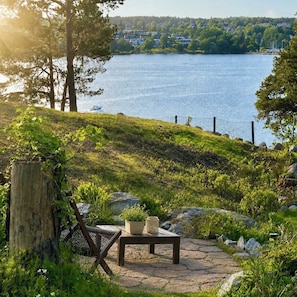 A patio with a chair and table, overlooking a lake with houses in the background. - Modern Seaside Guesthouse with Stunning Archipelago Views (Stockholms län)