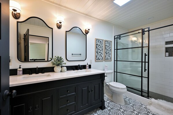 A modern bathroom with a black vanity, white sink, and a glass shower enclosure.