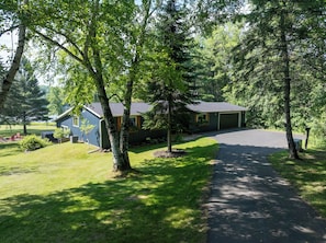 A two-story house with a garage, surrounded by a well-maintained lawn and trees. - Modern Lakehouse Retreat on Lake Namakagon With Private Hot Tub (Cable)