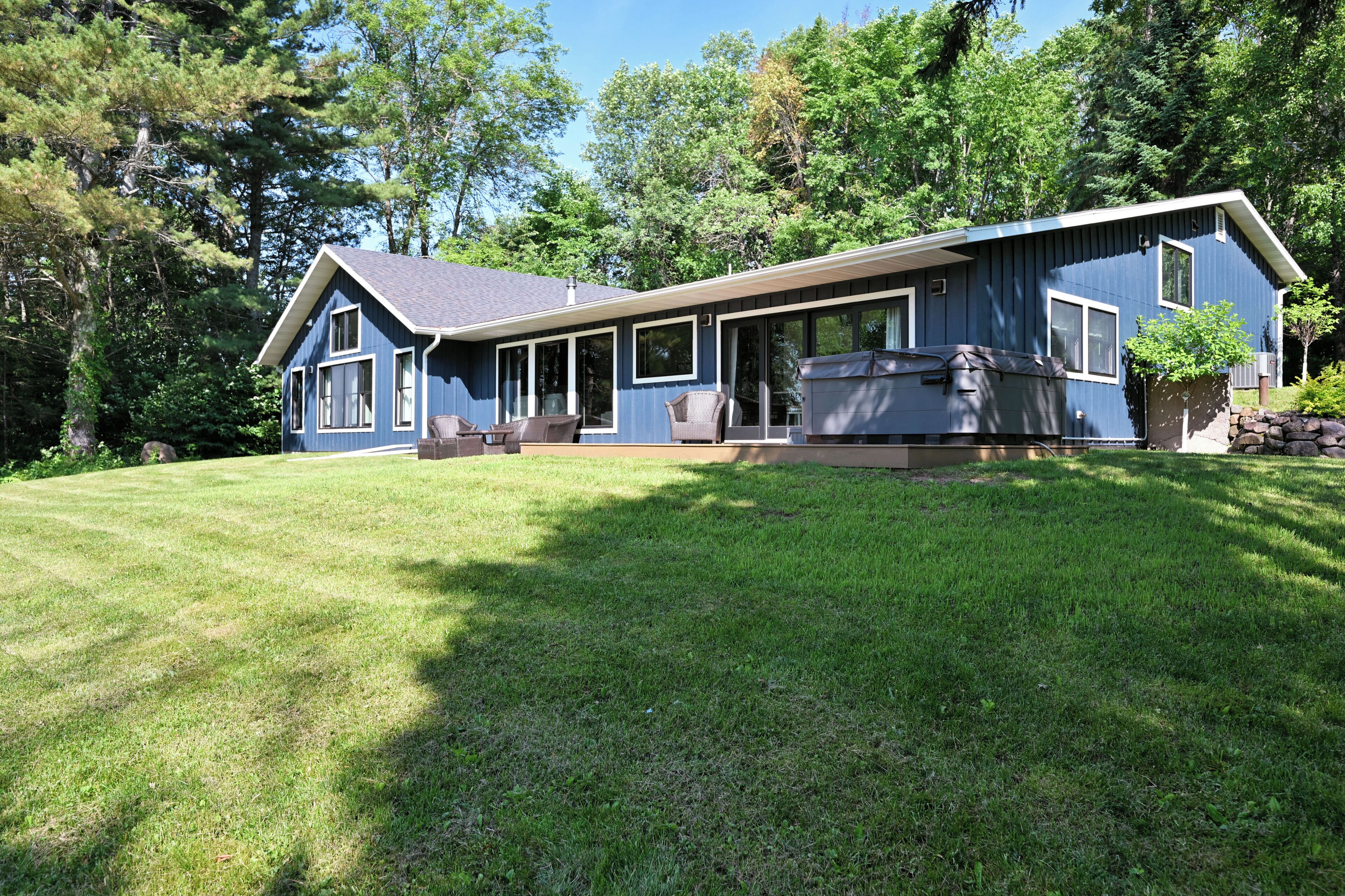 A two-story house with a large deck, a hot tub, and a well-maintained lawn.