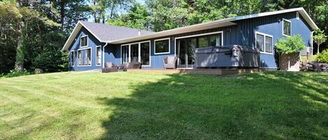 A two-story house with a large deck, a hot tub, and a well-maintained lawn.