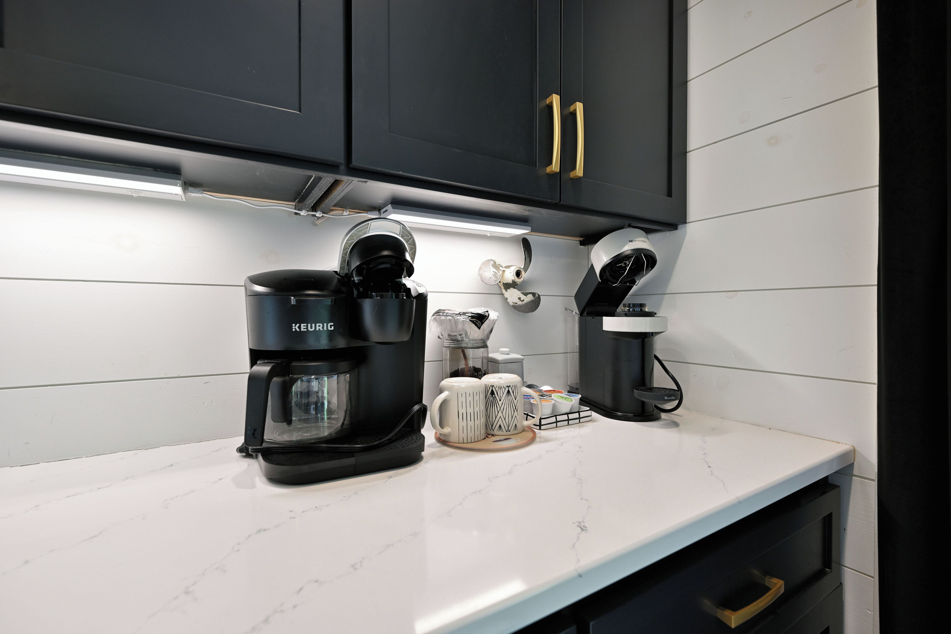 Una cocina con una cafetera Keurig, un molinillo de café y dos tazas sobre una encimera de mármol.