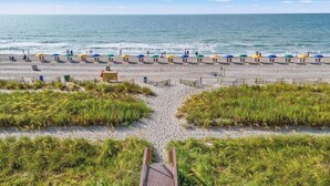 A beach with rows of colorful umbrellas and a wooden walkway leading to the water.