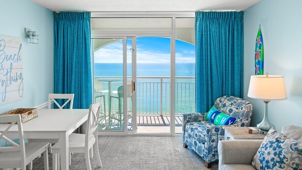 A room with a view of the ocean, a table with chairs, a sofa, and a lamp.
