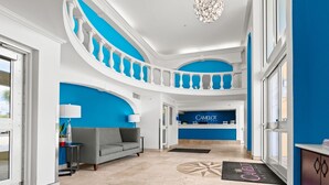 A hotel lobby with a blue accent wall, a reception desk, a chandelier, and a grey sofa.