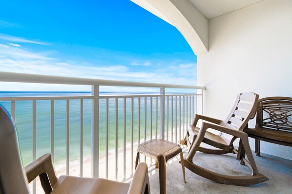 A balcony with a view of the ocean, a rocking chair, a lounge chair, and a small table.
