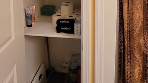 A closet with folded towels, makeup items, and a small stool.