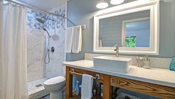 A bathroom with a shower, toilet, vanity with a mirror, and a sink.
