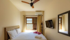 Egy szállodai szoba, amelyben található egy ágy, egy mennyezeti ventilátor, ablakfüggönnyel ellátott ablak, egy a falra szerelt televízió és egy radiátor.