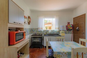 Une cuisine compacte équipée d’un four à micro-ondes, d’un four et d’un évier. On y trouve une fenêtre avec des rideaux, une porte et une table recouverte d’une nappe à motifs.