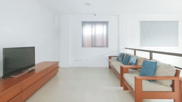 A modern living room with a flat-screen TV on a wooden stand, a sofa set with cushions, and a window with curtains. - RedDoorz @ Qhouzz near PUP (Manila)