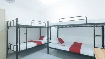 A dormitory room with bunk beds, a fan, and a door.