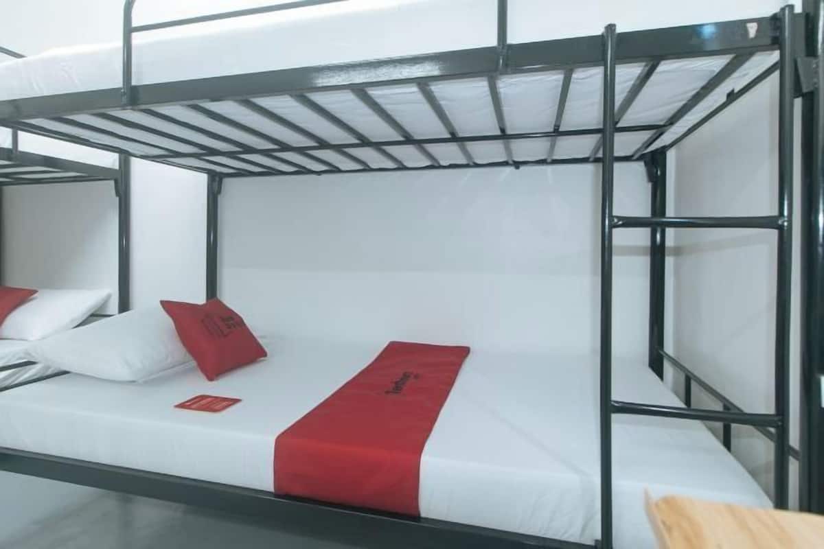 Dormitorio con literas, ropa de cama blanca y detalles rojos, incluyendo almohadas y una manta.