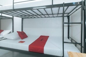 Dormitorio con literas, ropa de cama blanca y detalles rojos, incluyendo almohadas y una manta.
