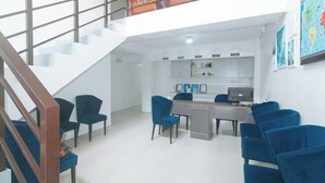 A modern hotel lobby with a staircase, a reception desk, and blue chairs. - RedDoorz @ Qhouzz near PUP (Manila)