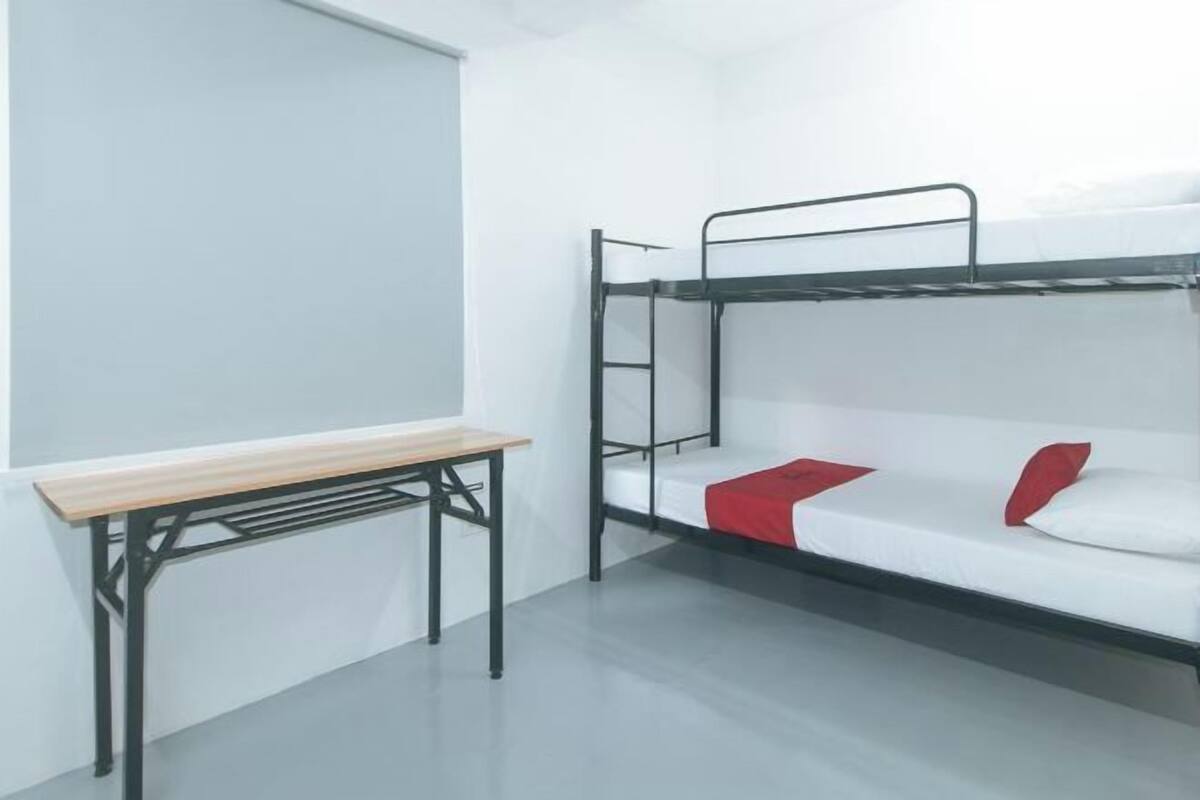 Una cama litera con un almohadón rojo, una mesa de madera y una ventana.