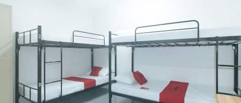 A dormitory room with bunk beds, a fan, and a wooden bench.