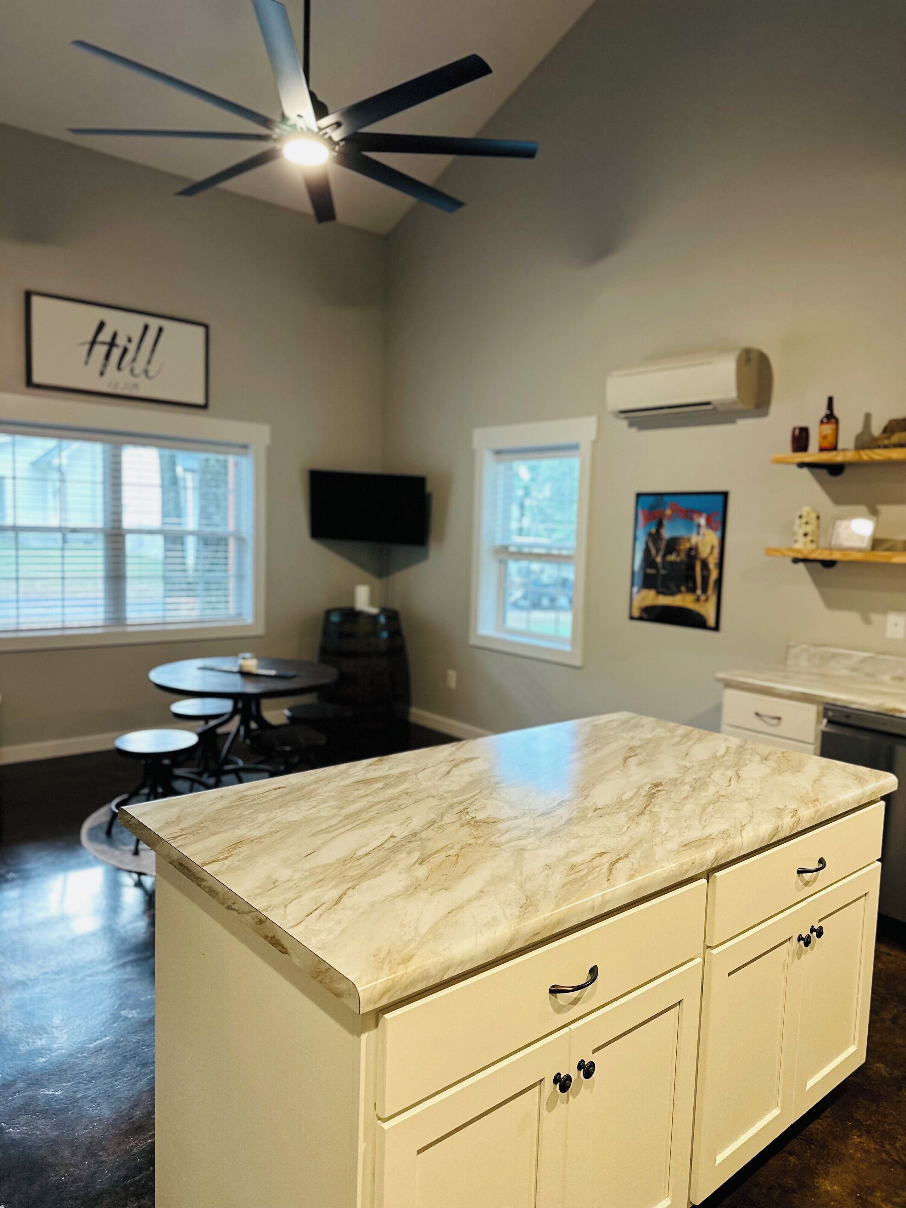 A kitchen with a marble countertop, white cabinets, a ceiling fan, and a dining area with a table and chairs.