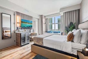 A modern hotel room with a large bed, a desk with a computer, a TV, and a window with a city view.